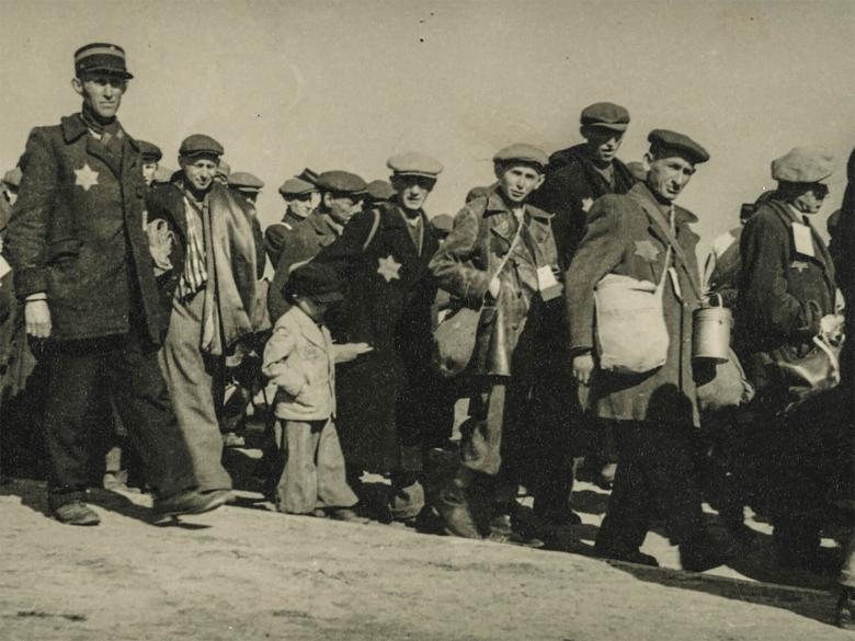detail of historical black-and-white photograph depicting a column of Jewish men and children, some with visible Stars of David on coats