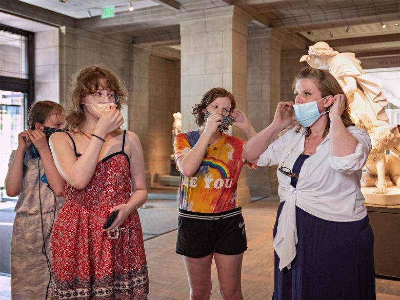Four visitors putting on masks at Huntington Avenue Entrance
