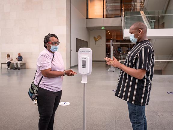 Two visitors applying hand sanitizer on their hands near hand sanitizer dispenser