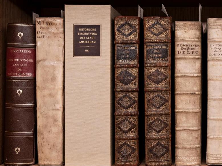 The spines of several old Dutch and Flemish books that sit on a shelf.