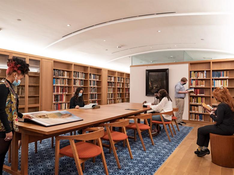 People congregate around a table in a library and flip through books.