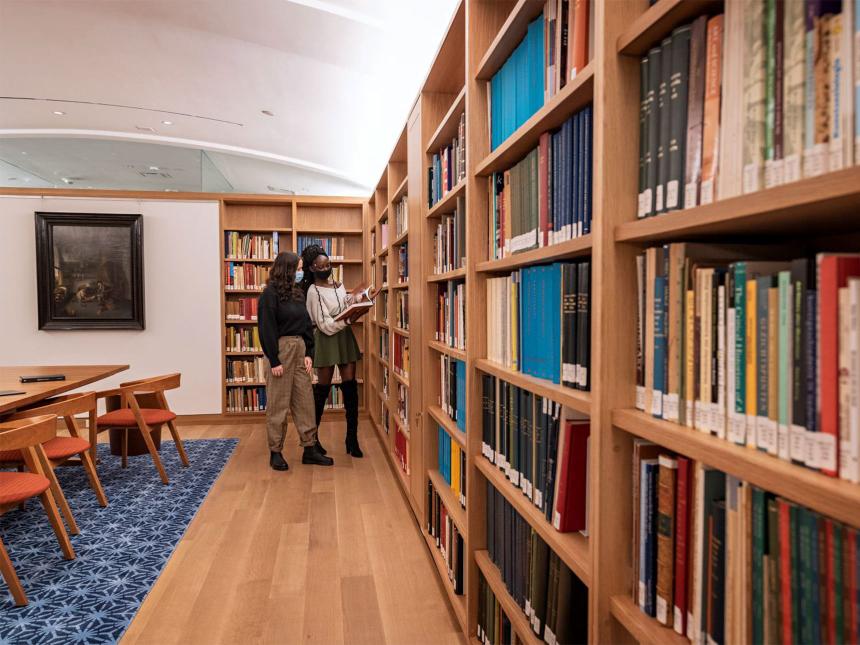 two young visitors looking at a book while standing next to long row of bookshelves