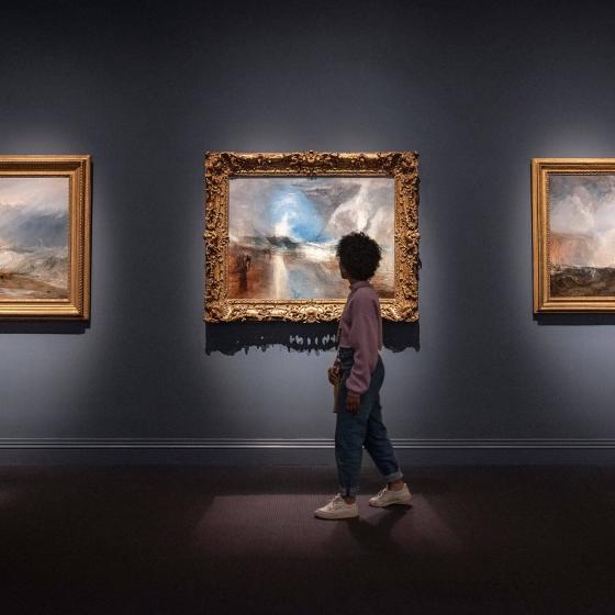 Visitor walking past framed JMW Turner painting depicting impressionistic view of storm over shoreline