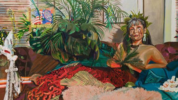 A figure wrapped from the waist down in a red patterned textile reclines surrounded by green plants.