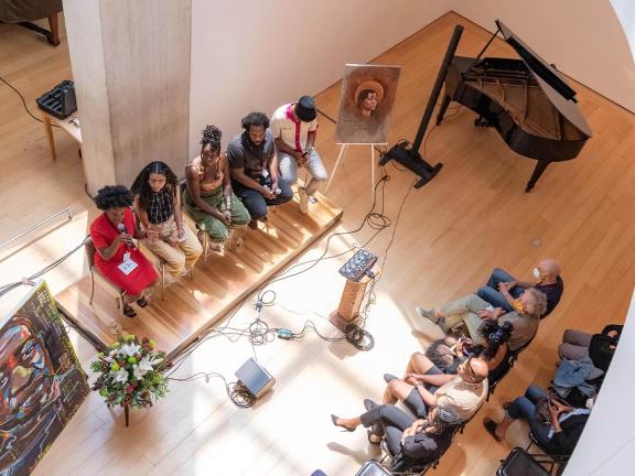 Overhead view of five panelists sitting on a stage in front of an audience and between two paintings