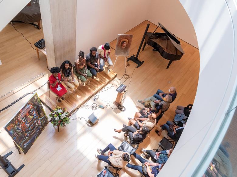 Overhead view of five panelists sitting on a stage in front of an audience and between two paintings