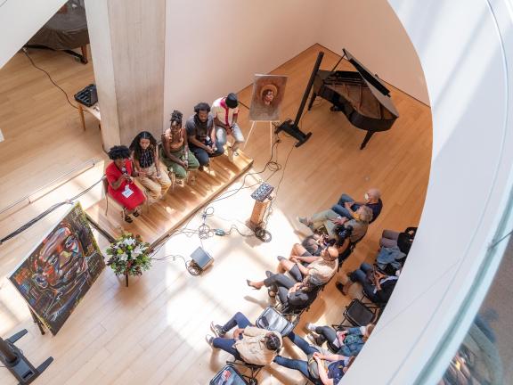 Overhead view of five panelists sitting on a stage in front of an audience and between two paintings