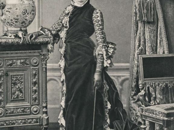 A photo of a woman standing in a long velvet gown and leather gloves. 