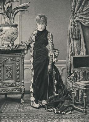 A photo of a woman standing in a long velvet gown and leather gloves. 