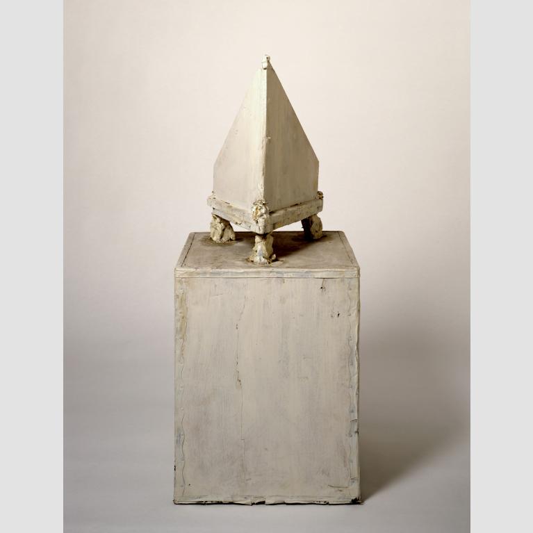 A rectangular prism sculpture topped with a pyramid-shaped sculpture on legs. 