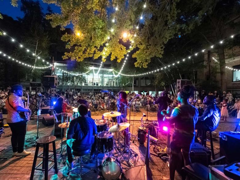 A band performs in the Calderwood Courtyard in front of a crowd at night.