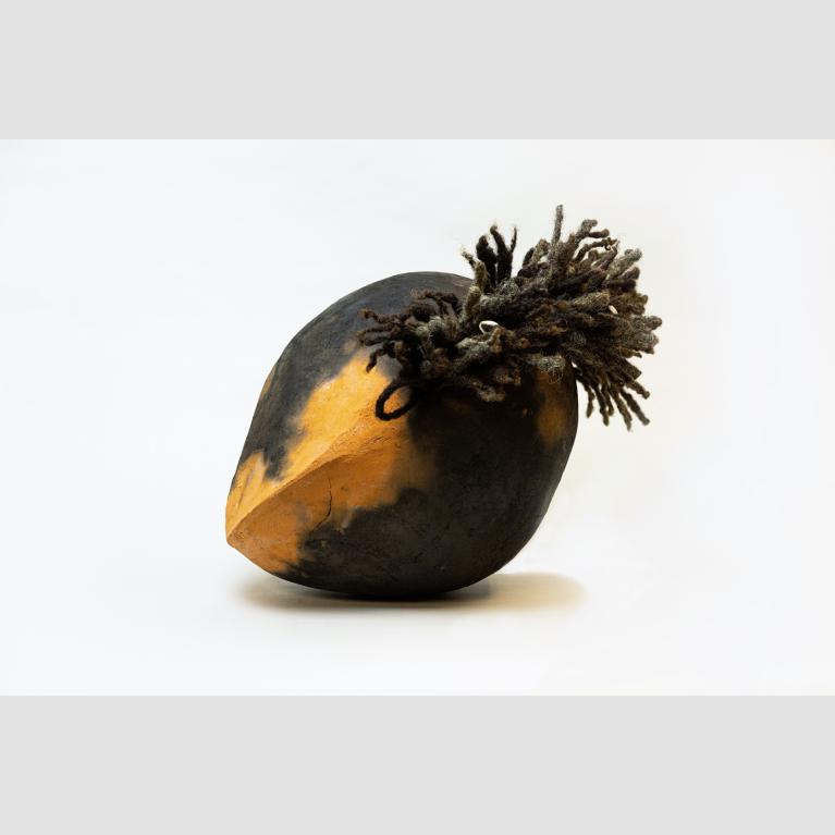 Orange black cemetery soil is molded into a mango shape and punctured with real human hair.