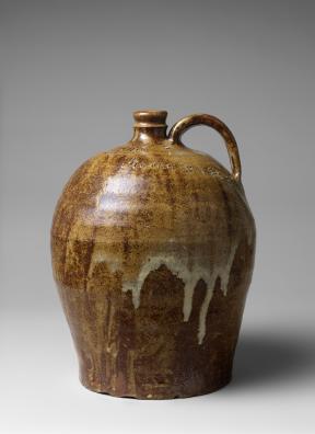A large, clay jug of brown hues with white drips, a handle, and small opening.