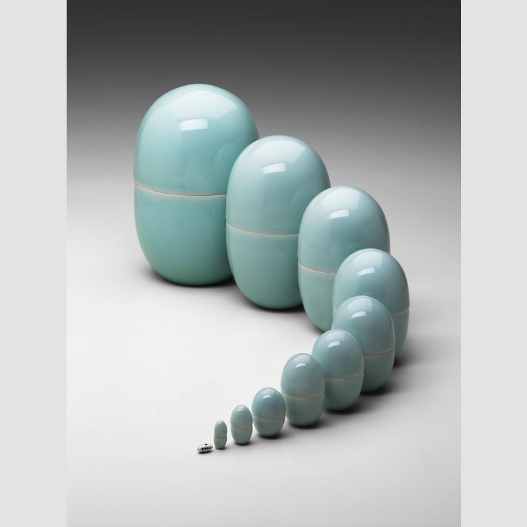 Eleven light-blue porcelain oval-shaped nesting boxes lined up in a curve and increasing in size from one to the next.