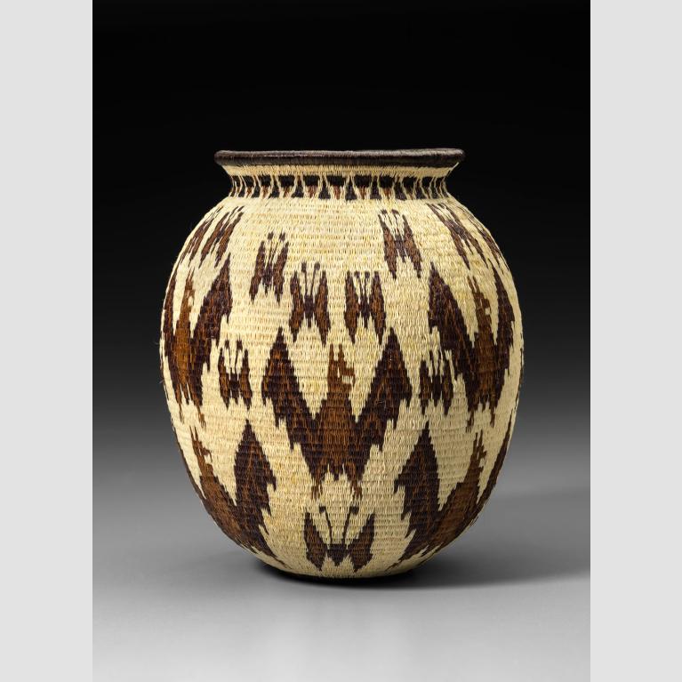 A beige basket woven from plant fibers and dyed with a brown pattern. 