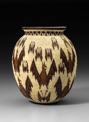 A beige basket woven from plant fibers and dyed with a brown pattern. 
