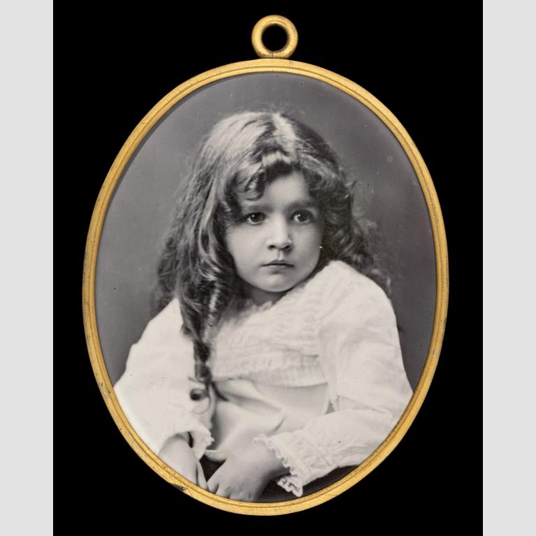 A black-and-white enamel photo of a young girl in a gold oval frame. 