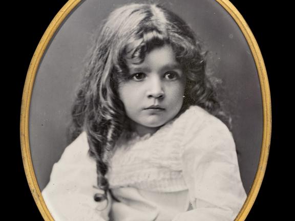 A black-and-white enamel photo of a young girl in a gold oval frame. 