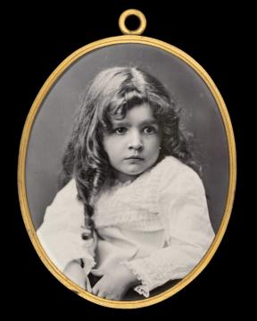 A black-and-white enamel photo of a young girl in a gold oval frame. 