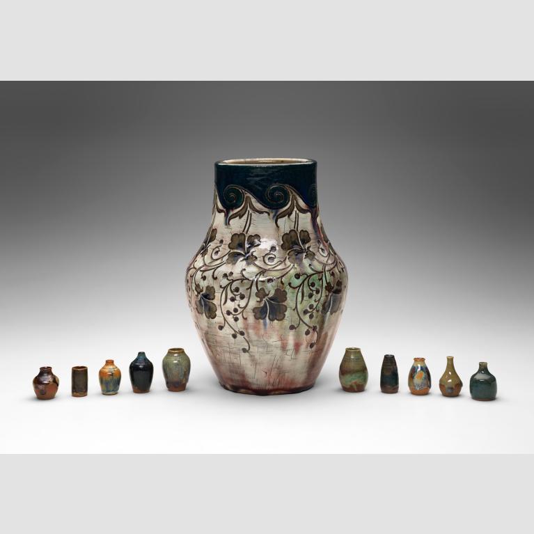 A large stoneware vase is flanked by five smaller vases on either side.