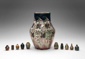 A large stoneware vase is flanked by five smaller vases on either side.