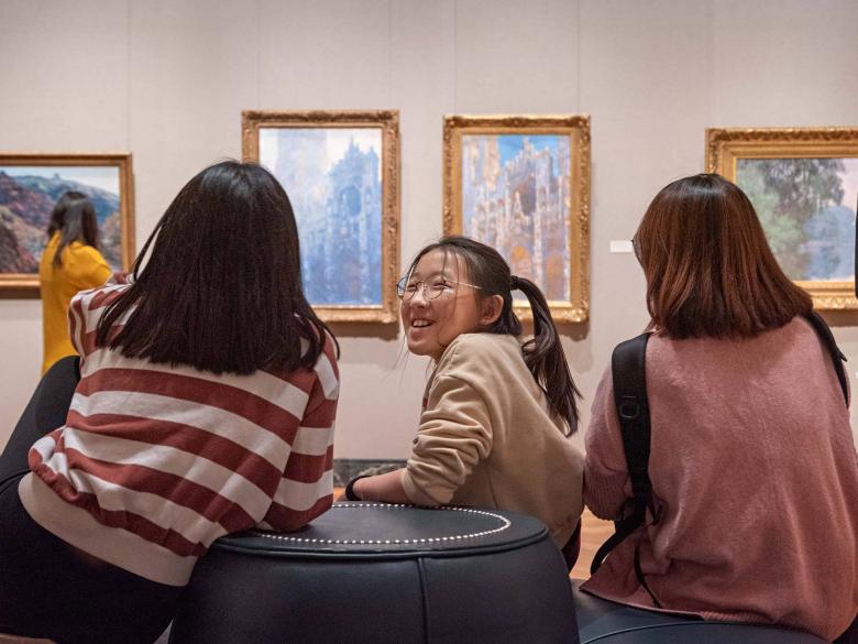 Three visitors chatting on a round couch in Impressionism gallery