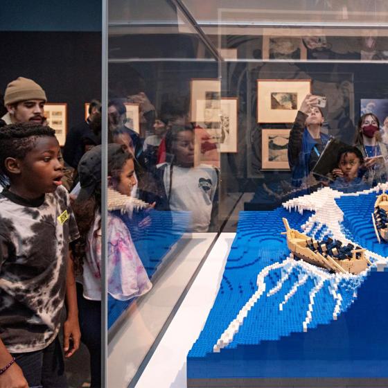 A group of visitors gather around a LEGO replica of Hokusai's "Great Wave."
