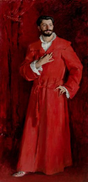A man in a bright red robe stands against dark red velvet with his left arm akimbo and tight hand at his chest.
