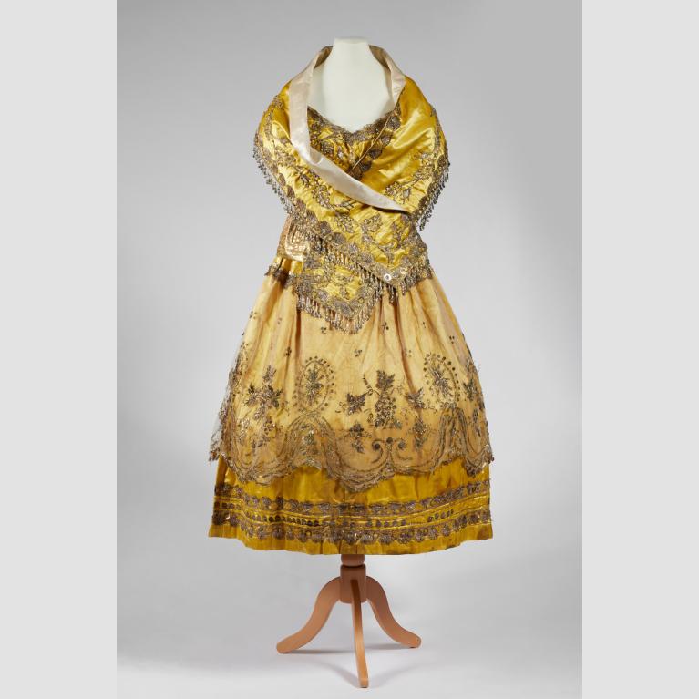 A yellow, beaded dress and scarf combination placed on a mannequin. 