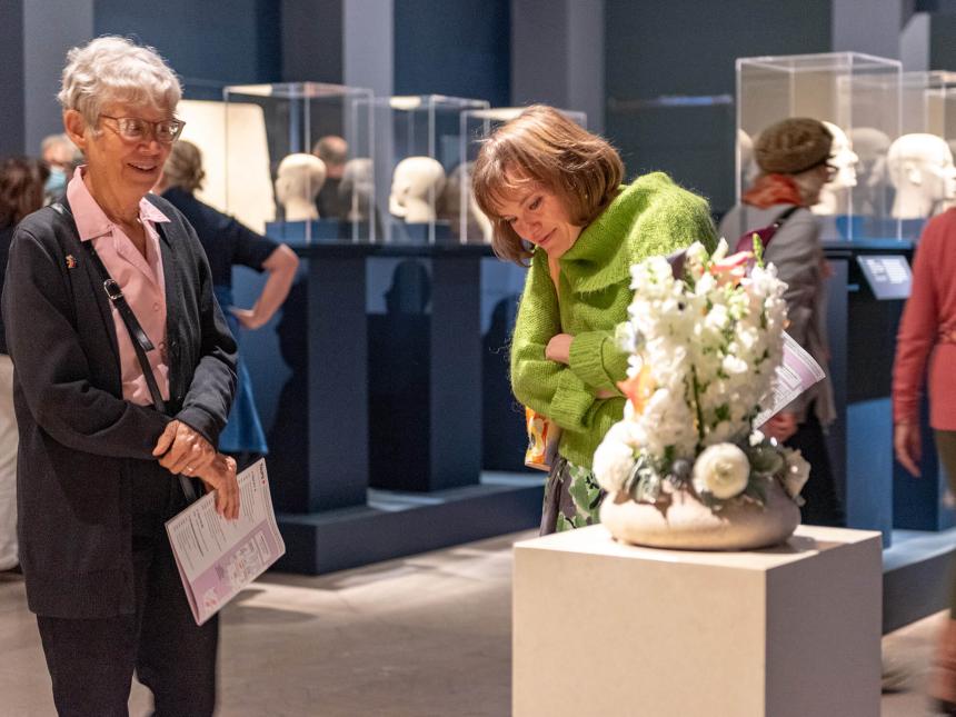 Two visitors in Egyptian gallery, looking at arrangement of white flowers in low, round vase