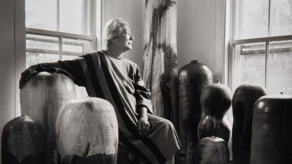 Artist Toshiko Takaezu sits among her works of pottery and looks out the window.
