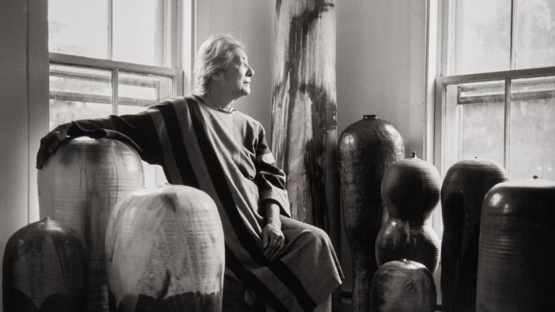 Artist Toshiko Takaezu sits among her works of pottery and looks out the window.