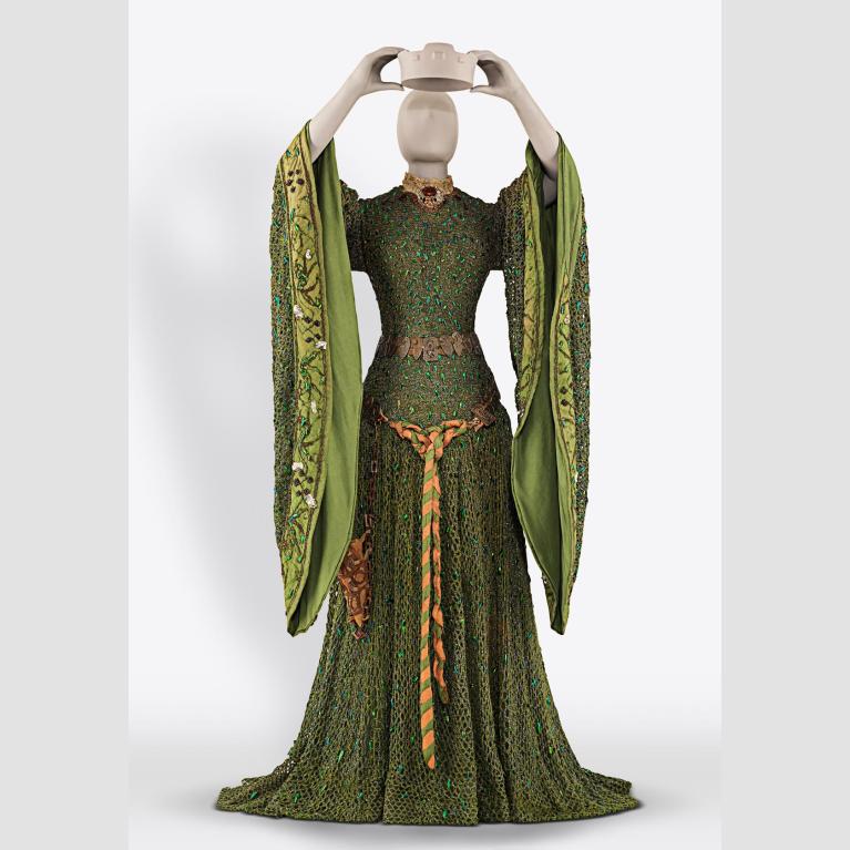 A mannequin wears a green dress with wide sleeves and golden belt. 