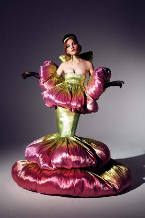 A model poses in a pink and green dress that poofs out at the mid-arms, waist, and feet.