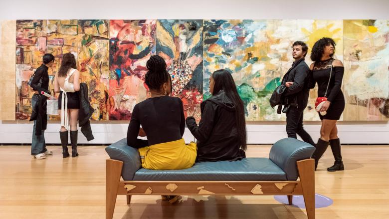 Visitors in evening attire sitting and standing in front of multi-paneled abstract painting with different patterns on each panel
