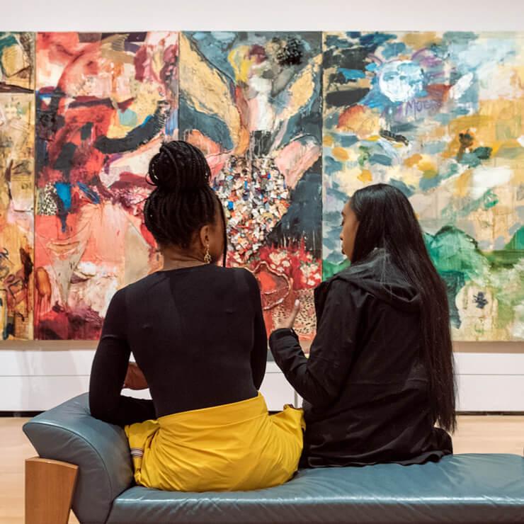 Visitors in evening attire sitting in front of multi-paneled abstract painting with different patterns on each panel