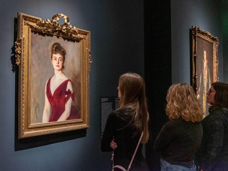 Visitors looking at Sargent painting of Mrs. Inches, a woman in red sleeveless dress