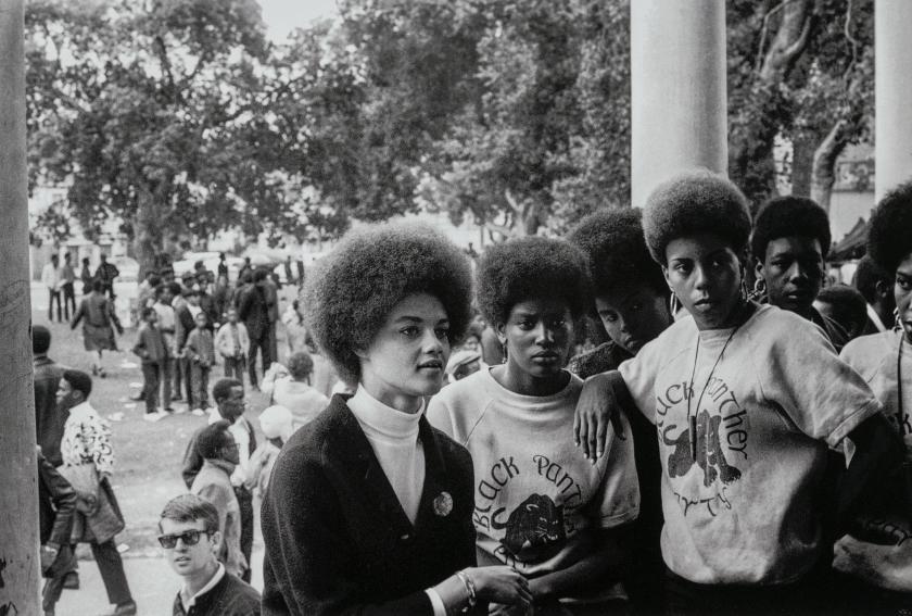 Black-and-white photo: a group of Black women look off into the distance as they stand before a crowd gathered on a lawn.