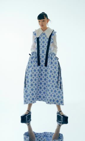A model wears a white and blue apron dress with black ribbon details.