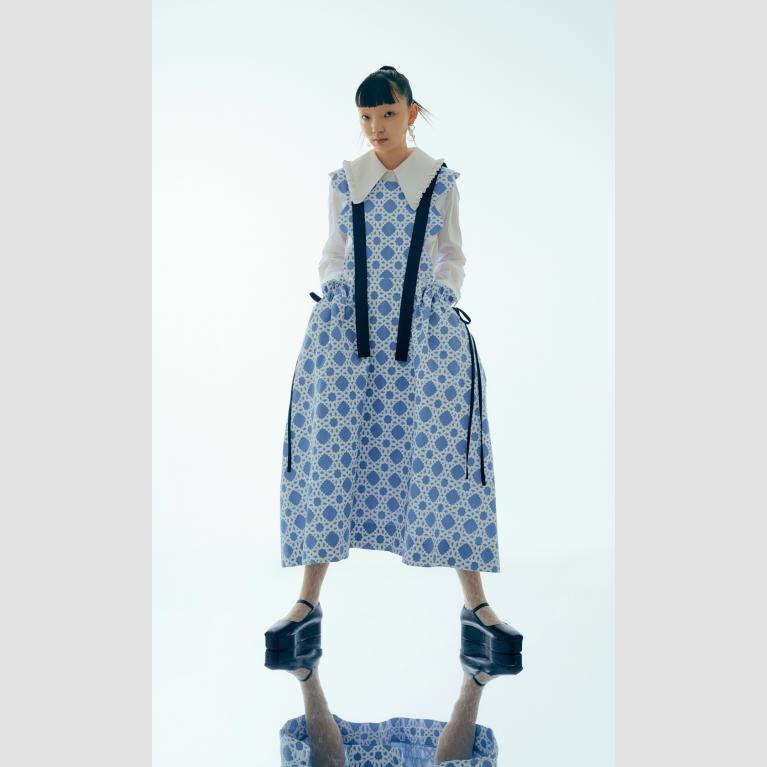 A model wears a white and blue apron dress with black ribbon details.