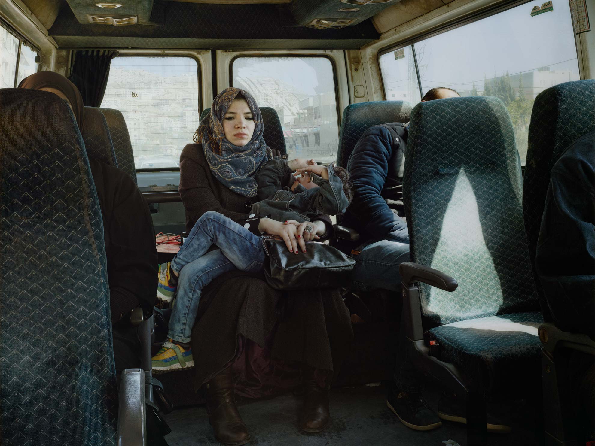 Luc Delahaye, Taxi, depicting a woman with a head covering who holds a writhing child in the back seat of a taxi cab as sunlight streams in through the window.