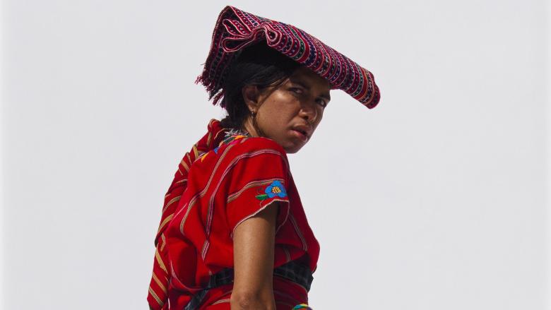 Print depicting a person in an ornate red outfit stands with their back to the camera and looks over their shoulder.