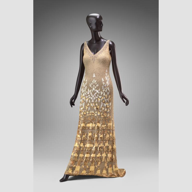 A mannequin wears a silk gold embellished dress. 