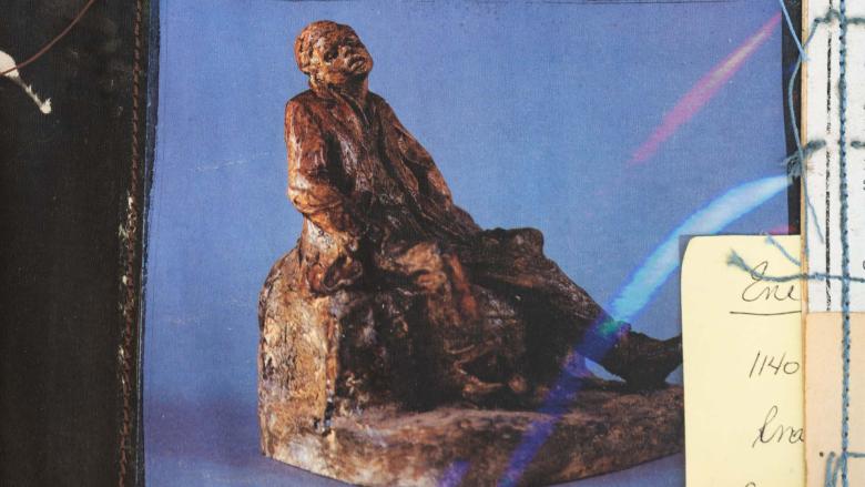 A sculpted figure of a person with eyes closed and moth open sitting on a rock.
