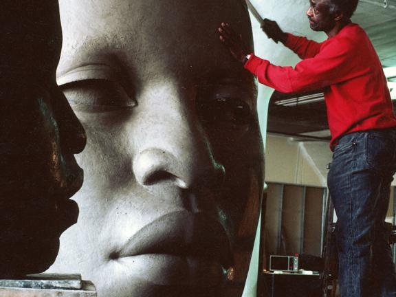 John Wilson working on clay sculpture head with African-American features and closely cropped hair 