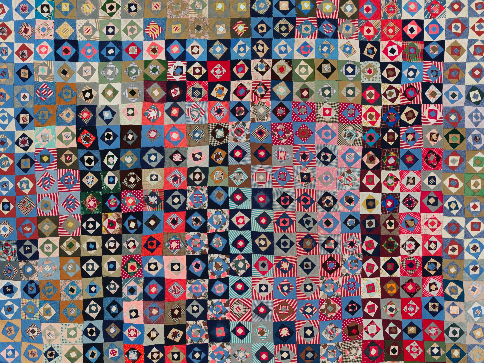A colorful, intricate, and geometric patchwork quilt in reds, blues, blacks, and greens
