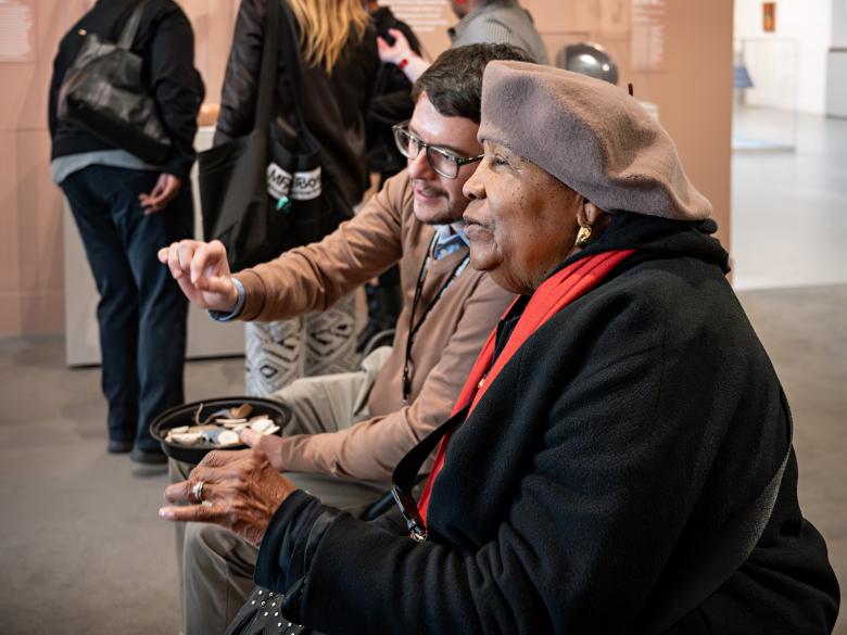 Two participants in an access program chat on a bench in a gallery