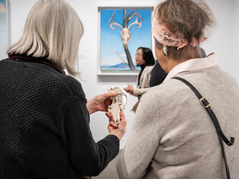 Tactile access tour with two people touching a small skull in front of a Georgia O'Keeffe painting