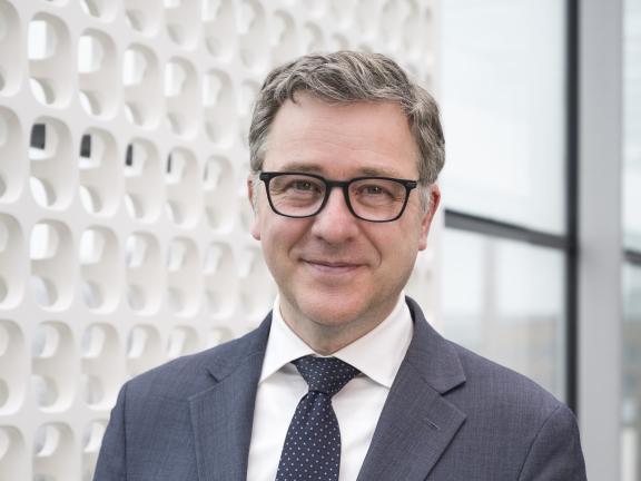 Pierre Terjanian in gray suit and dotted tie standing in hallway filled with natural light