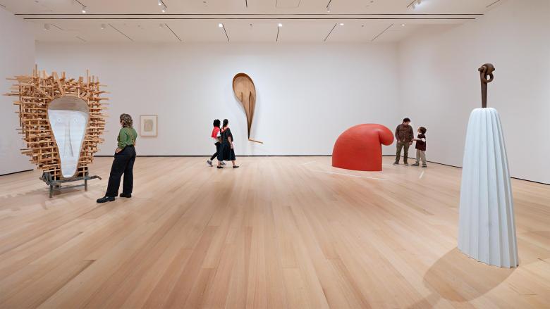 Wide view of gallery featuring various sculptures by Martin Puryear, including one made of wooden beams resembling portal and another that looks like a giant gnome's hat